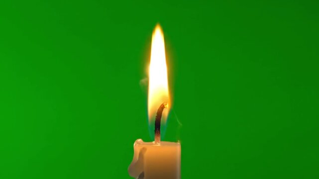 Lit candle with bright flame on green background