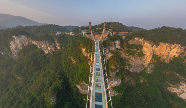 Aerial view of the thrilling Glass Bridge stretching between rocky cliffs covered in lush green vegetation, a testament to human engineering, Glassbridge, Zhangjiajie, China.