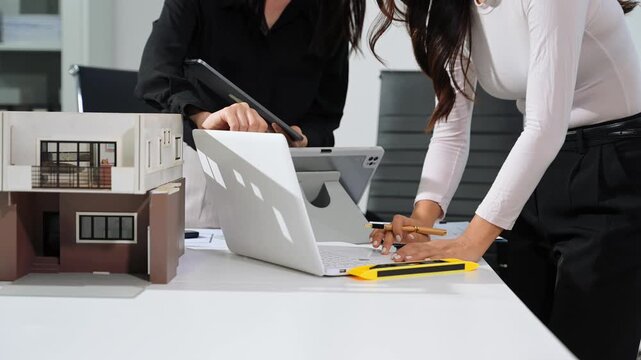 Professional architects using laptop and tablet beside modern house model, digital architecture planning, construction project management and real estate development concept.