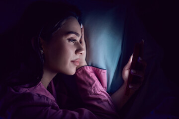 Fototapeta premium Close up of young woman using smartphone in dark bedroom. Concept of private messaging, mobile banking apps, secure login, digital privacy and individual screen time habits.