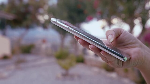 Young Woman Standing Outdoors in Modern Cottage Village Using Smartphone and Searching Online Information