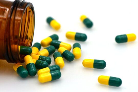 Green and Yellow Tramadol Capsule Pills Spilling Out of Brown Bottle on White Background