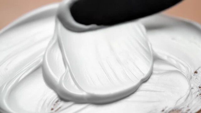 Close up of white cream being smoothly spread with a metal spatula on a surface