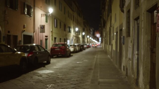Blurred florence street at night with soft bokeh streetlights, defocused parked cars, cobblestone pavement and aged stone facades background; background backplate copyspace template.