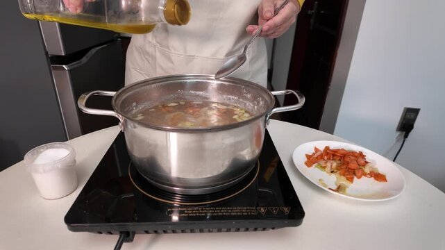A woman cooks soup on an induction hob, adds sunflower oil to the soup