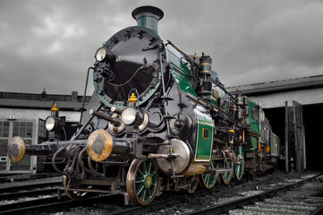 Obraz premium Impressive historic steam locomotive of the S 3/6 class of the Royal Bavarian State Railways in classic green paintwork from 1918. The restored machine stands in front of the depot shed.