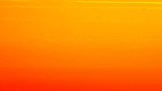 Sunset sky orange gradient glow with flying small birds creating an atmospheric, dramatic natural background.