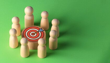 Goal driven team of wooden peg figures standing around red target symbol showing determination to succeed business challenge