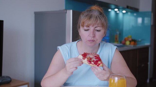 A woman eats a slice of pizza with gusto, sitting at the kitchen table at home