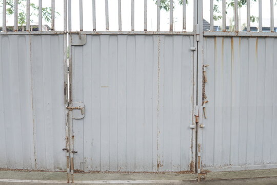 Weathered grey metal warehouse gate with rusty hinges, industrial fence, and secure latch detail.