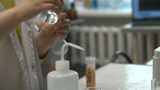 Carefully Adding Clear Solvent Into Round Flask Over Beaker In Welllit Laboratory Environment . Stock clip