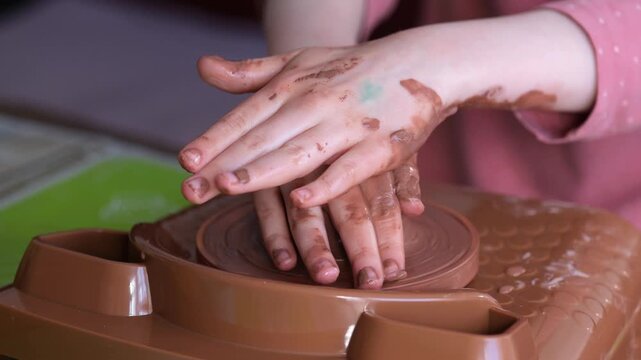 Children's palms squeeze and align the clay mass on the circle, the beginning of the formation of the future potty. A lively creative process in the workshop. The atmosphere of the craft.