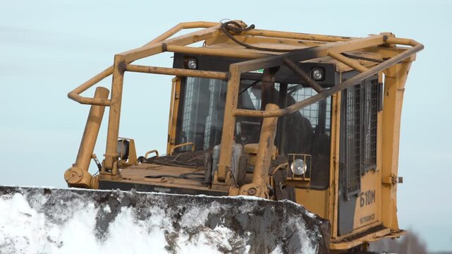 Heavy Steel Bulldozer With Hydraulic Arms Actively Clearing Snow In Cold Industrial Environment . Stock clip