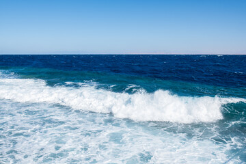Blue ocean waves crashing against the shore under a clear sky, showcasing the beauty of coastal waters and natural scenery