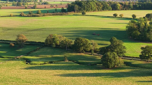 Tractor moving along rural road with farm implement during fieldwork period. Agricultural vehicle traveling through countryside route with attached equipment during seasonal operations. Farming
