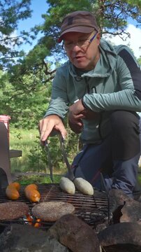 Young couple grilling sausages and burgers over campfire in sunny forest. Authentic outdoor culinary experience, sustainable living and mental wellness in a Finnish national park.