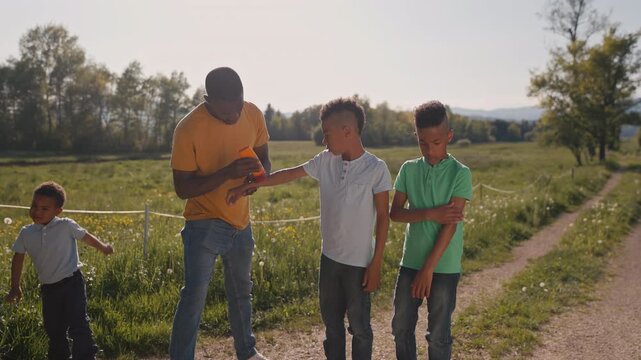 African American man, a father of three sons, ensures his kids are protected from the sun during a summer trip by applying sunscreen to them