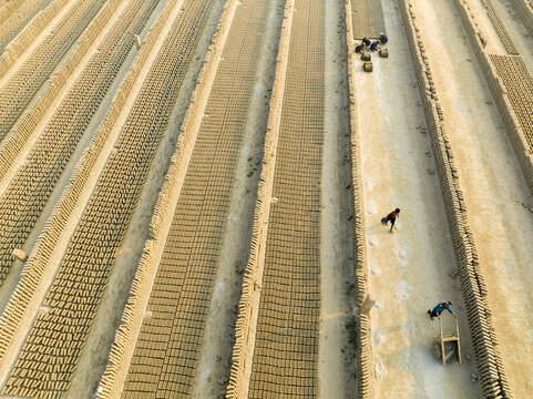 Aerial view of rows of sun-baked bricks stretching across the landscape, with workers moving along the sandy paths, Aminbazar, Dhaka Division, Bangladesh.