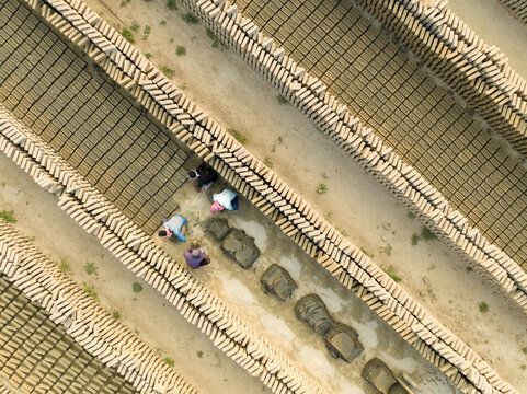 Aerial view of workers toiling amidst stacks of sun-baked bricks, creating rhythmic patterns against the earth-toned landscape, Aminbazar, Dhaka Division, Bangladesh.