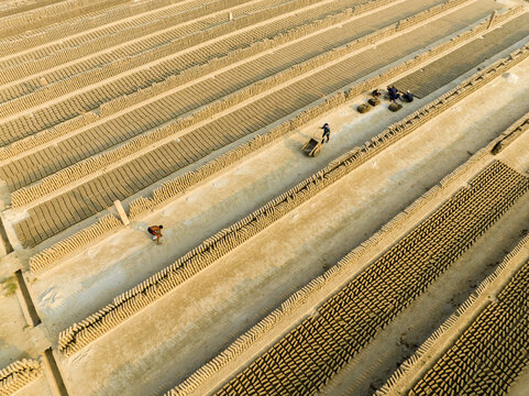 Aerial view of uniform rows of drying bricks create a textured landscape under the sun's golden light, Aminbazar, Dhaka Division, Bangladesh.