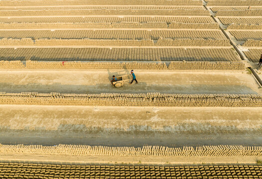 Aerial view of rows of bricks baking under the sun, contrasting with the worker pushing a cart, Aminbazar, Dhaka Division, Bangladesh.