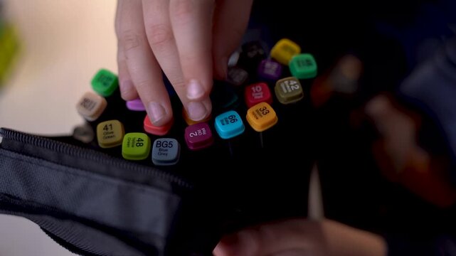 A hand sorts through colored markers with numbers in a black box
