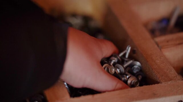 Close-up of a hand taking metal screws and driving them into a box