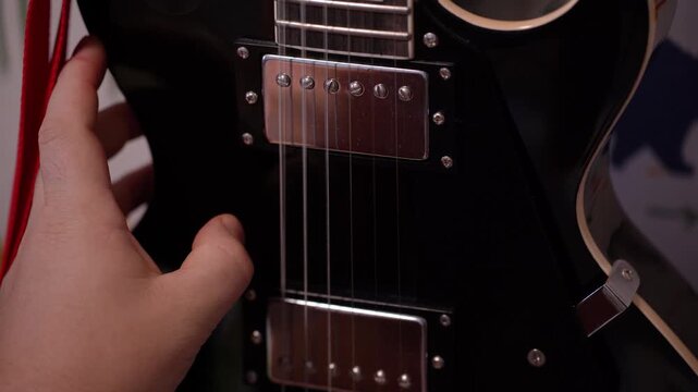 A musician's hand slides over the strings of a guitar hanging on the wall