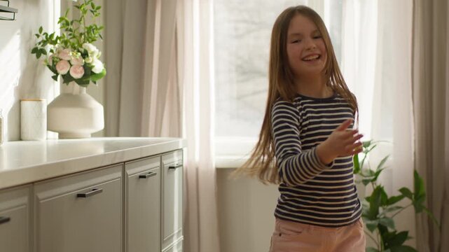 Cheerful hyperactive Caucasian little girl child kid daughter active dancing smiling happy at camera indoors dance at home moving to audio song music having fun energetic playful childhood family