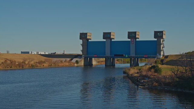 A scenic diagonal shot of the Blue Iwabuchi Sluice Gate. The modern floodgate and Arakawa River are captured with a sense of depth in Tokyo, Japan.