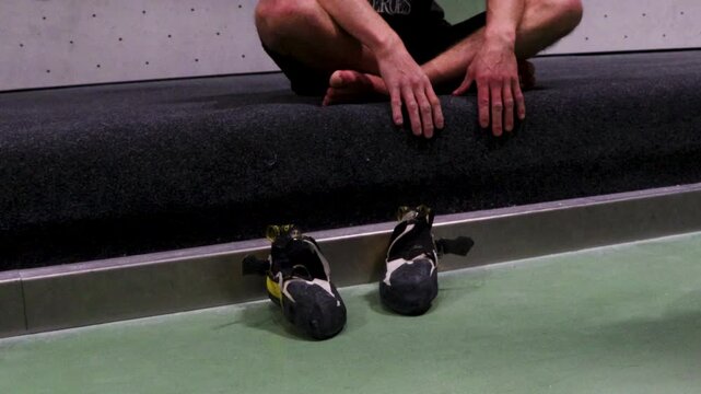 Video of person sitting down on a floor of a bouldering gym with shoes in front.