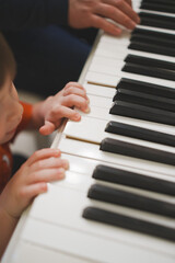 Fototapeta premium Child learns to play piano with adult during music lesson