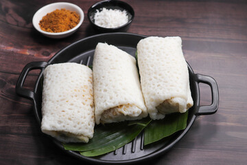 A closeup shot of a traditional Goan Alle Belle coconut pancakes. The crepes are rolled neatly and filled with a rich, dark brown mixture of grated coconut and palm jaggery. popular tea time snack.