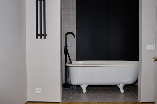 Vintage clawfoot bathtub standing in modern bathroom with black wall and tiled floor, no people visible, minimalist interior design emphasizing clean lines and functional layout