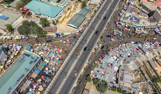 Aerial view of a bustling market sprawling beneath a concrete bridge, a vibrant tapestry of colorful umbrellas and bustling activity, Kano, Kano, Nigeria.