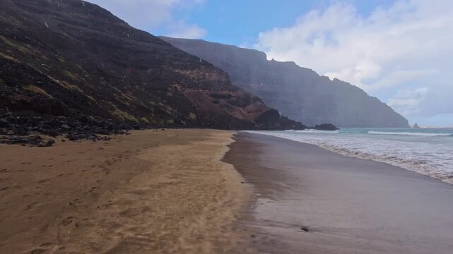 einsamer Strand am Fu&szlig;e dunkler Klippen im Regen, unber&uuml;hrte K&uuml;stenlandschaft, ruhige Brandung, Regenwetter, Regenschauer, Wolkenhimel, Lanzarote, Kanarische Inseln, Spanien, Reisen, Landschaft