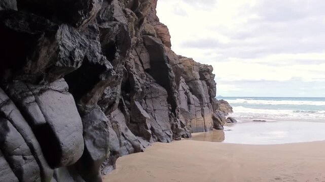 Impressive cliffs on an empty sandy beach, gentle waves washing over mighty rocks, calming atmosphere, dramatic sky, ideal backdrop for relaxation, vacation, sea, ocean, coast, travel, landscape

