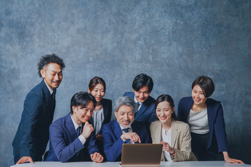 ノートパソコンの前に集合する様々な世代のスーツを着た男女