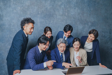 ノートパソコンの前に集合する様々な世代のスーツを着た男女