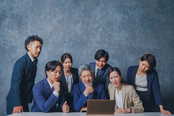 ノートパソコンの前に集合する様々な世代のスーツを着た男女