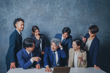 ノートパソコンの前に集合する様々な世代のスーツを着た男女