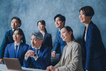 ノートパソコンの前に集合する様々な世代のスーツを着た男女