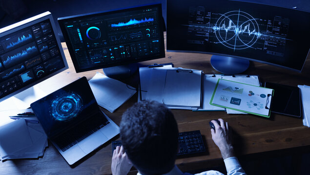 Strategic composition. Business analyst working with multi screen financial dashboards at night. Concept of market monitoring, data driven strategy and corporate performance analysis.