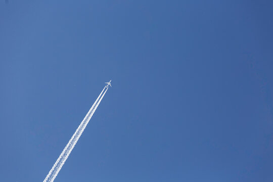 Passenger airplane flying at high altitude, leaving a long white contrail against a clear blue sky. Minimal composition with strong sense of direction