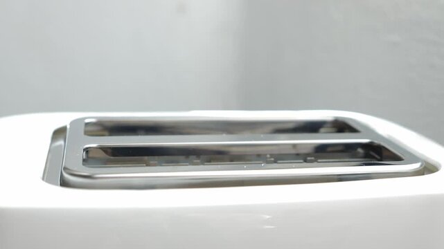 Two fresh slices of bread lowering into a modern white kitchen toaster to be cooked for a delicious breakfast, showing a simple and common household appliance in action on a white background