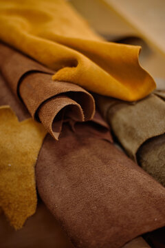 Closeup showing stacked brown and tan leather hides lying on workshop table, highlighting texture and natural grain, suitable for crafting handmade leather goods or accessories