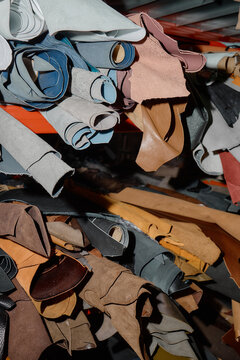 Stacks of assorted leather hides and rolled leather pieces arranged on workshop shelves, showing variety of textures and colors used for crafting and manufacturing leather goods