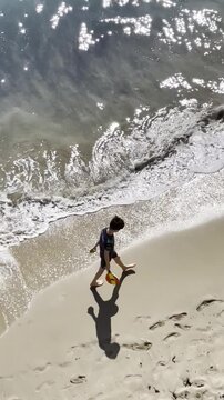 Ni&ntilde;o en playa con olas de mar, huellas descalzo, sombra y paseo con raqueta y pelota en verano