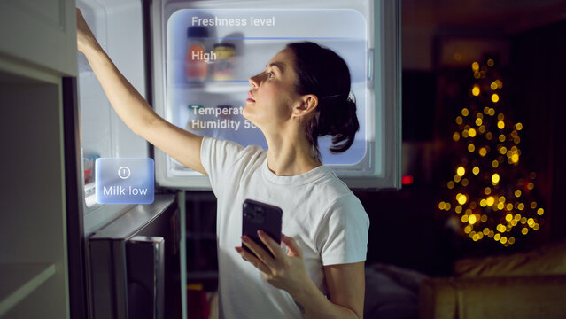 Woman checking smart refrigerator with freshness and humidity display. Concept of intelligent food storage, freshness tracking, inventory monitoring and connected home appliances.