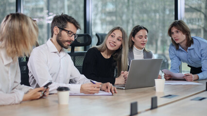 Obraz premium A group of people are sitting around a table with a laptop open